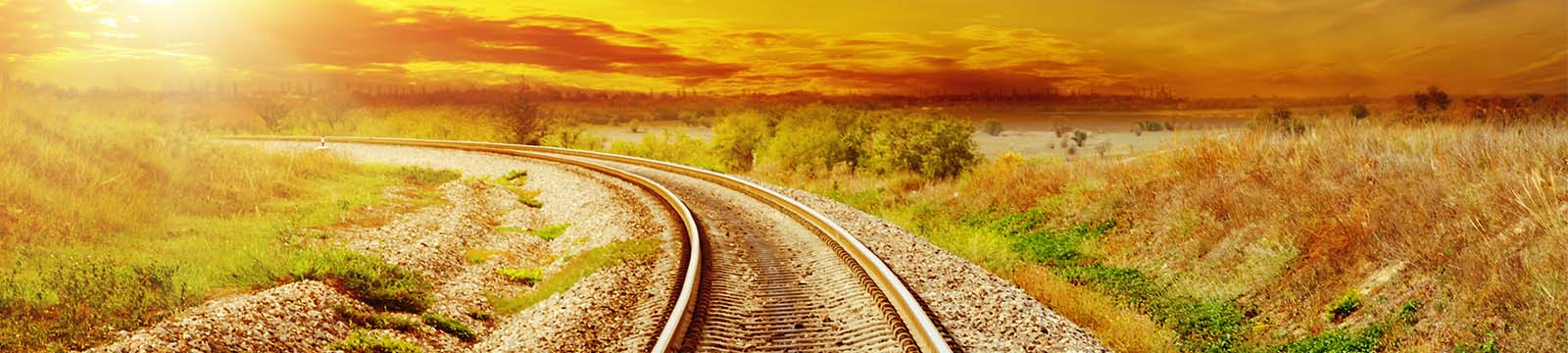 Train tracks running through the prairie curving towards a sunrise.