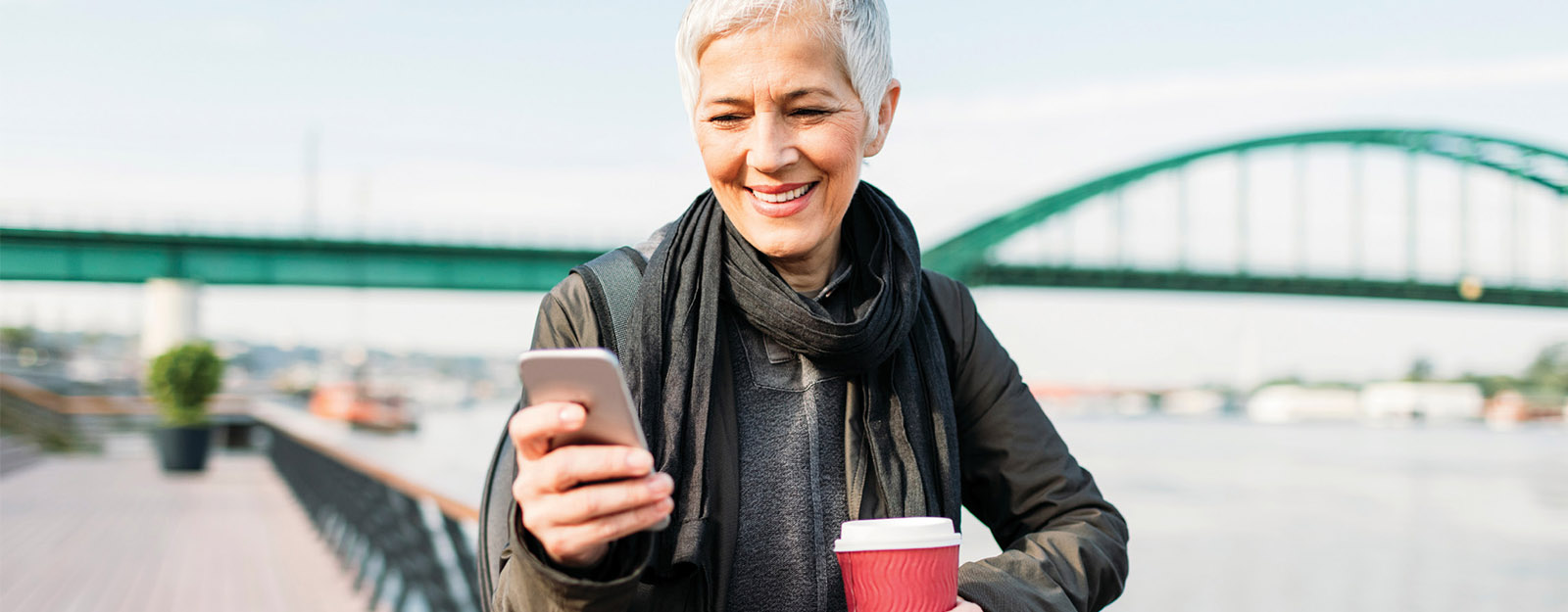 Image of woman site seeing while looking at her phone and holding a coffee.
