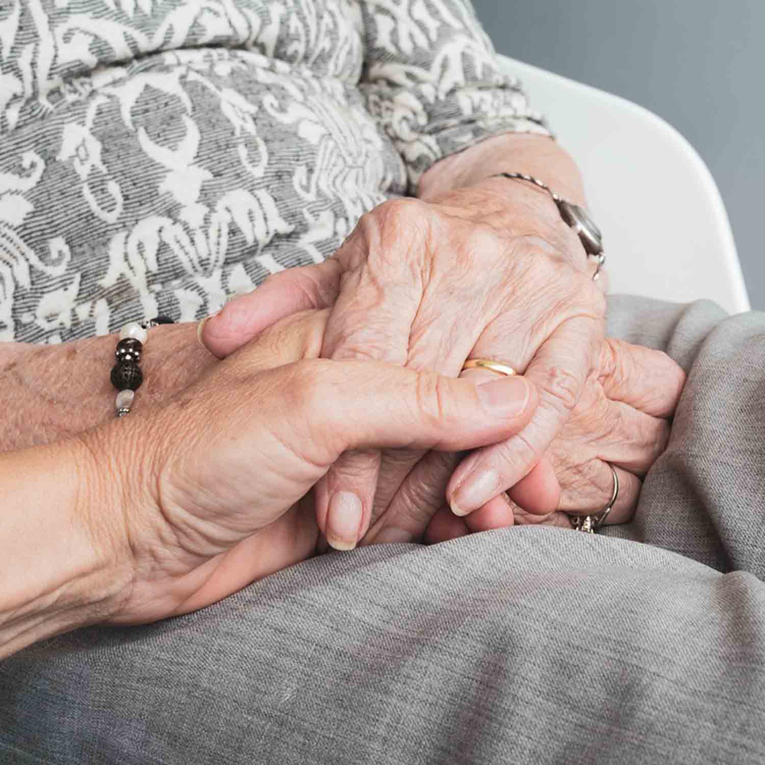 Close up photograph of an elderly person holding a younger individual's hand.