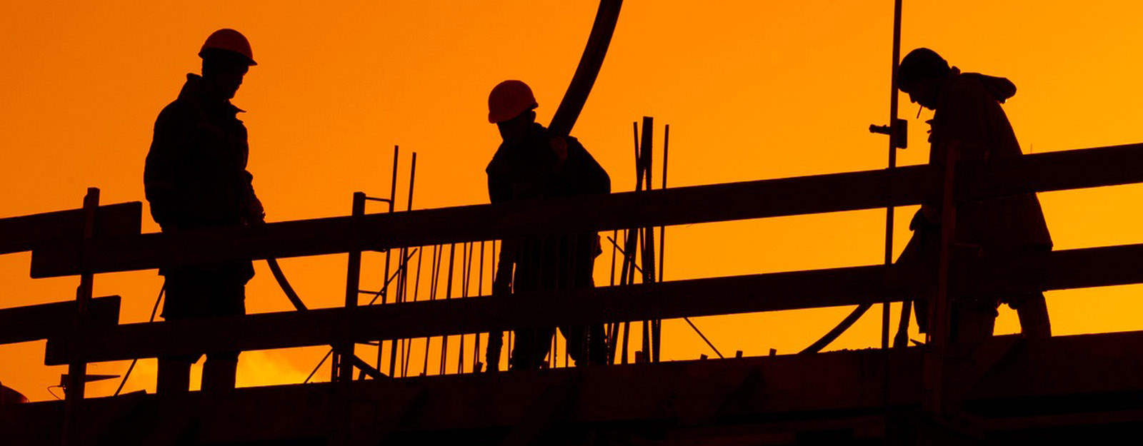 Silhouettes of three construction workers with a sunset in the background. 